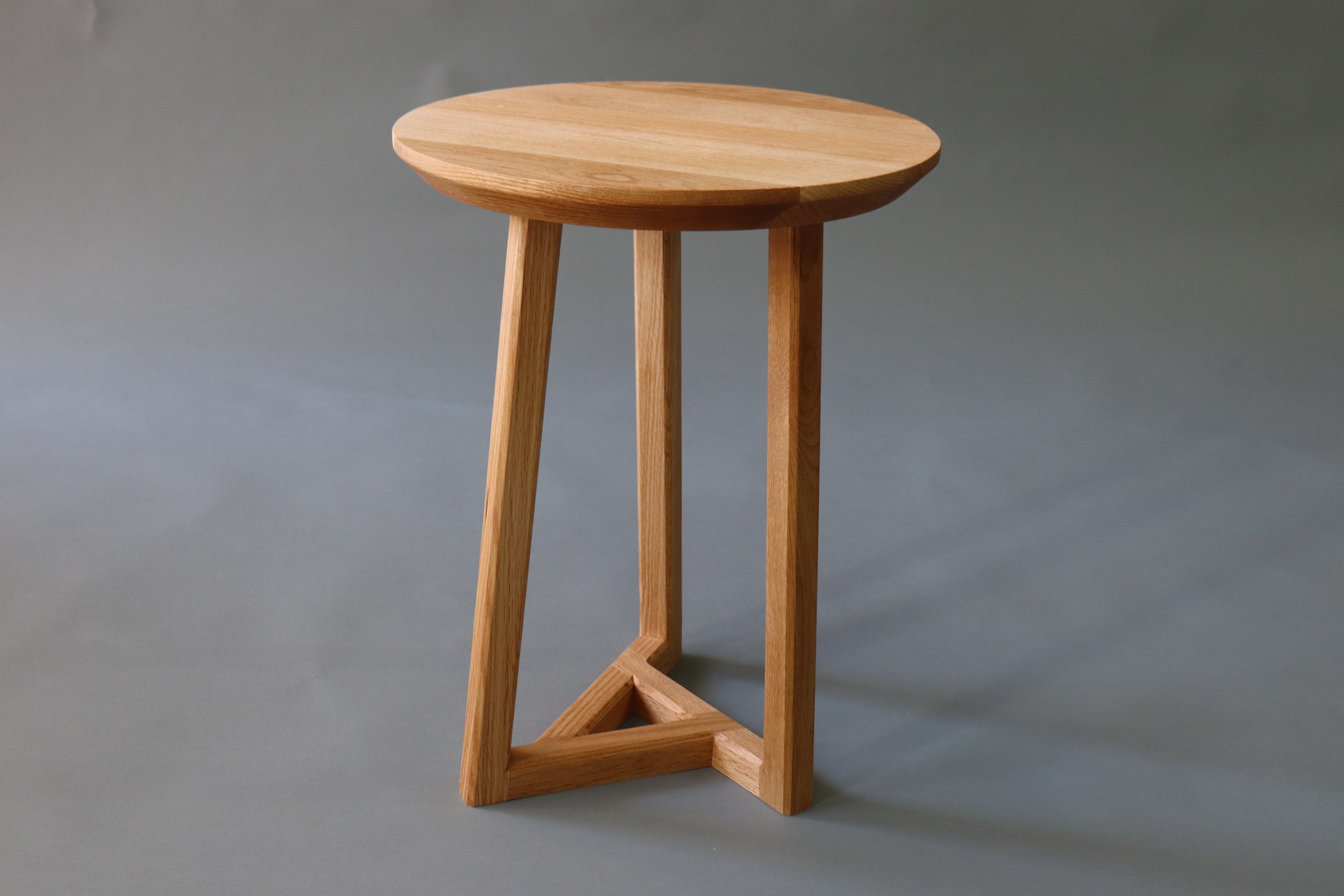 A small round wooden side table with three angled legs and a triangular base,