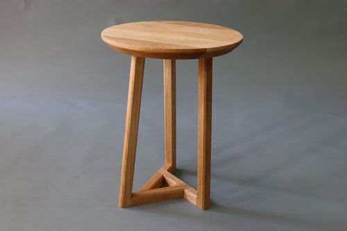 A small round wooden side table with three angled legs and a triangular base,
